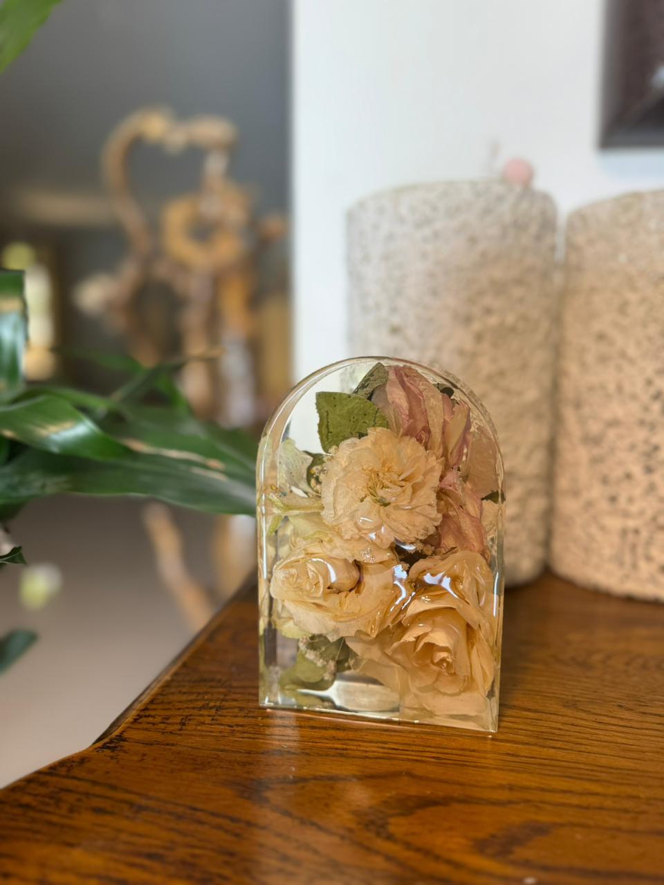 Full view of "Resin Arc Block by Hyacinth Arts featuring preserved cream-colored flowers encased in clear resin, displayed on a wooden surface with blurred background decor."