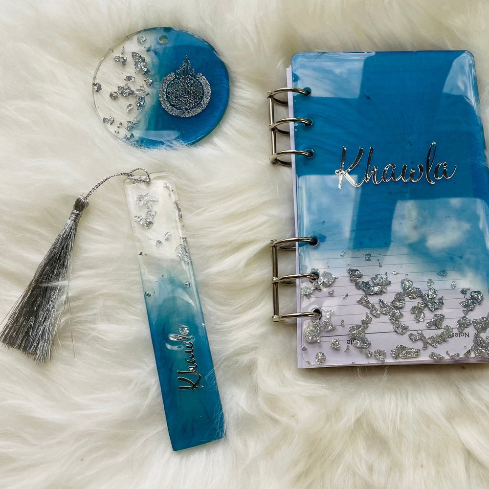 Top view of an ocean-themed resin bookmark, resin coaster, and ocean-themed book arranged on a soft feather-like surface, showcasing matching blue tones and glossy finishes.