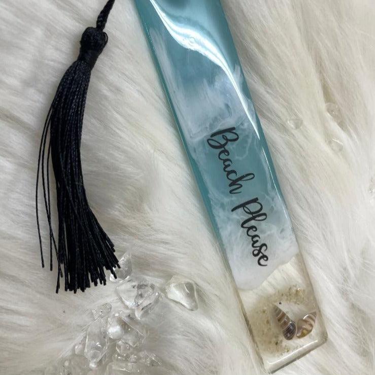 Top view of a single ocean-themed resin bookmark resting on a soft feather-like surface, displaying its vibrant blue waves and glossy epoxy finish.