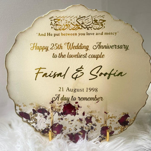 "Front view of a wedding and anniversary coaster displayed on a gold stand, set against a soft white feather-typed background, highlighting its elegant design and celebratory theme."